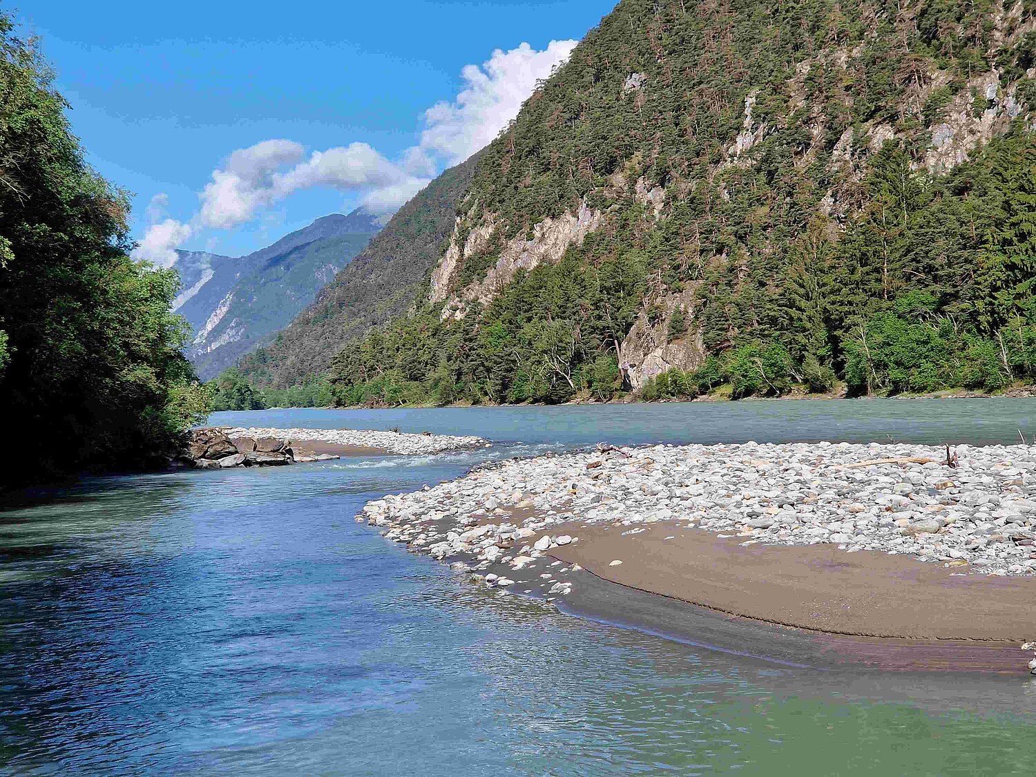 Der Fluss Inn mit einer Schotterbank zwischen bewaldeten Berghängen.
